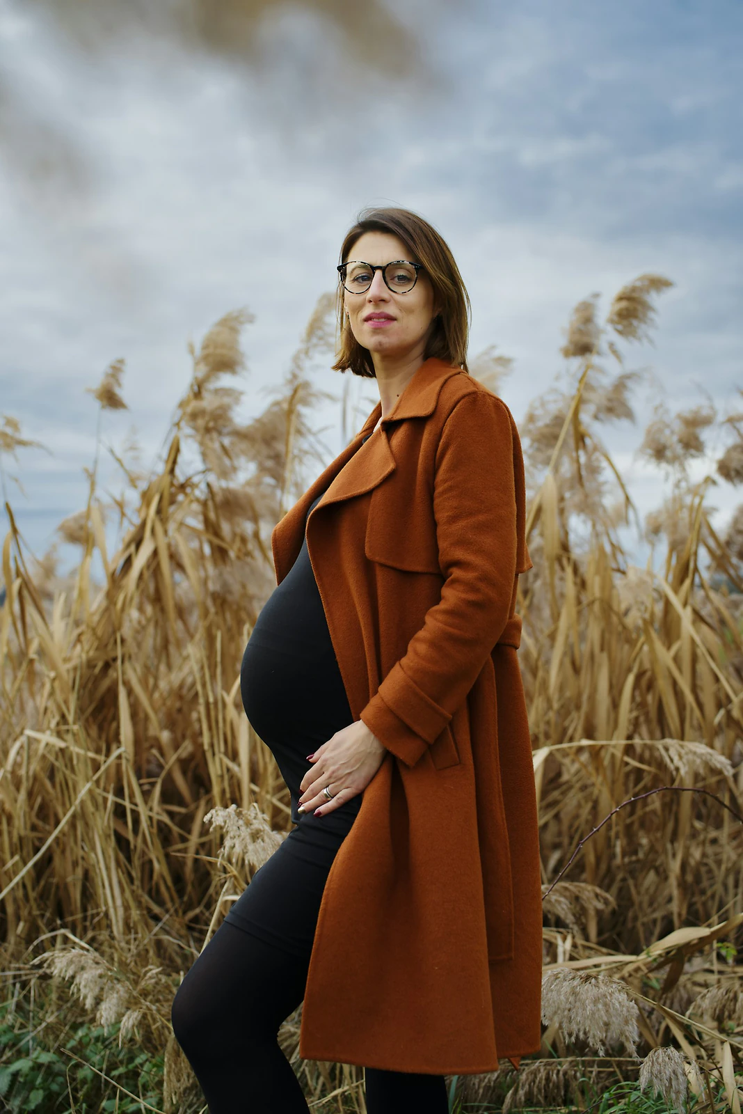 Pregnant woman in a flowing dress standing among tall grass in an open field