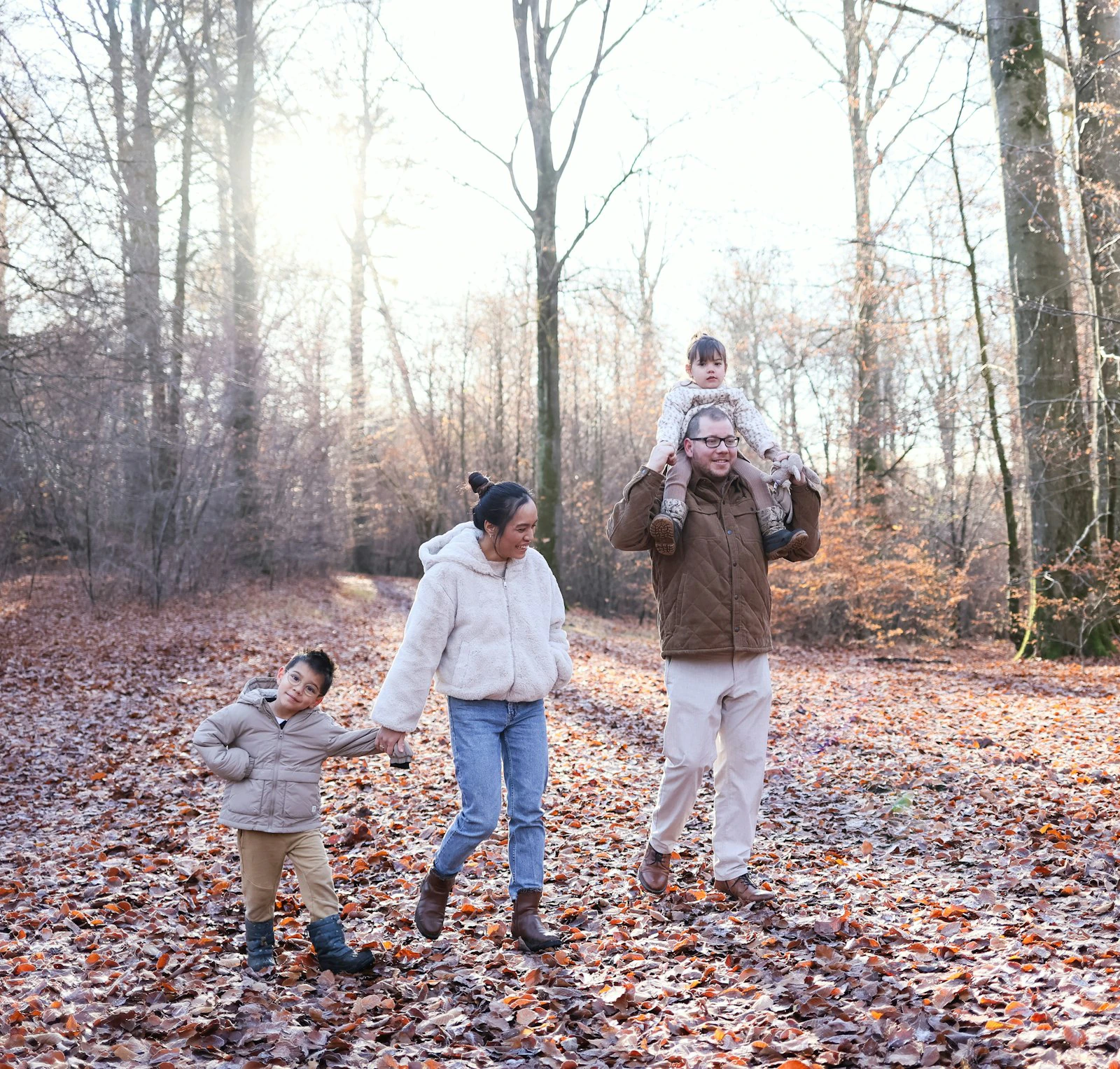 Family in layered jackets and warm textures walking a path covered in autumn leaves