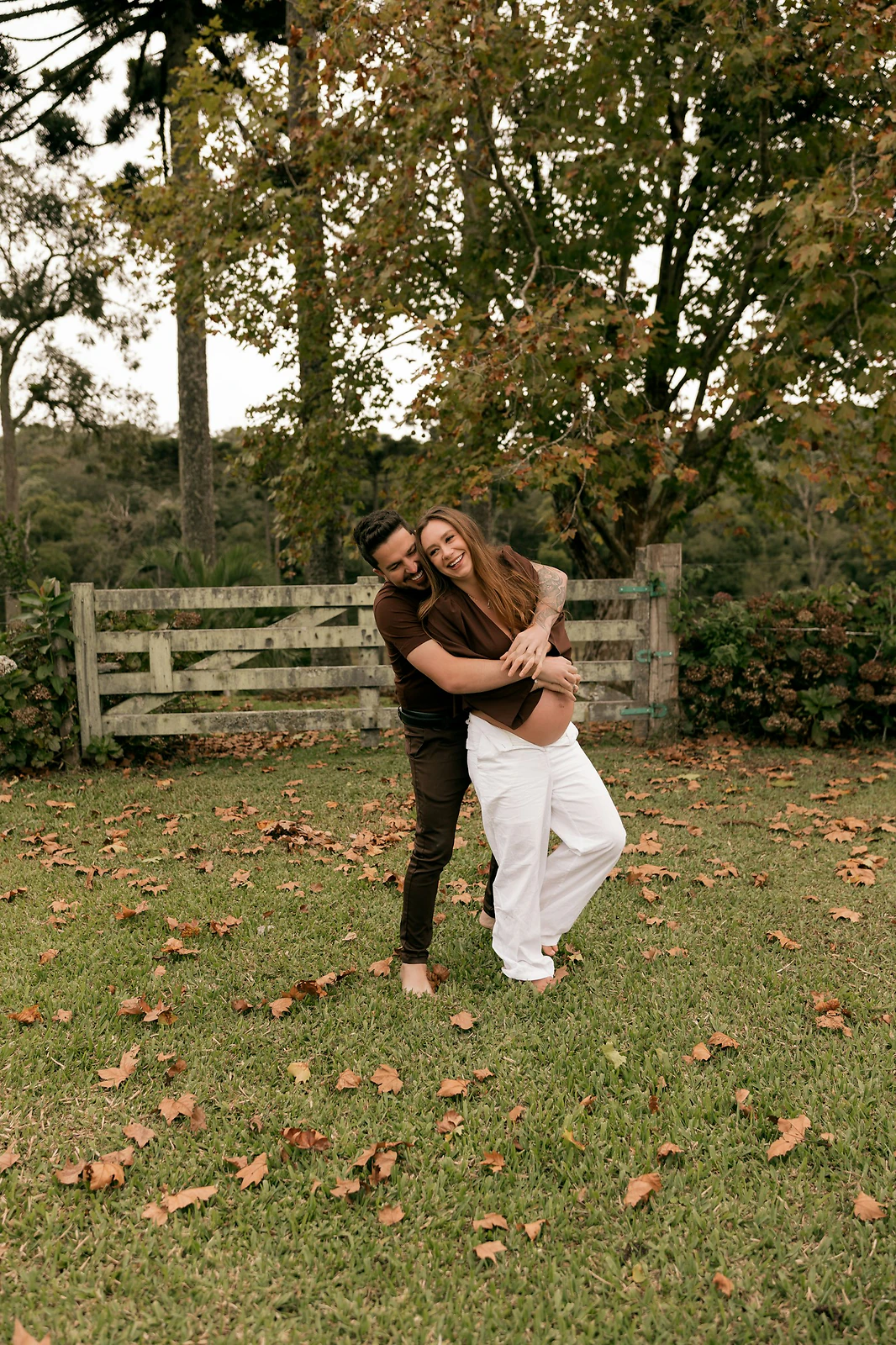 Expecting couple embracing in a field surrounded by golden autumn foliage