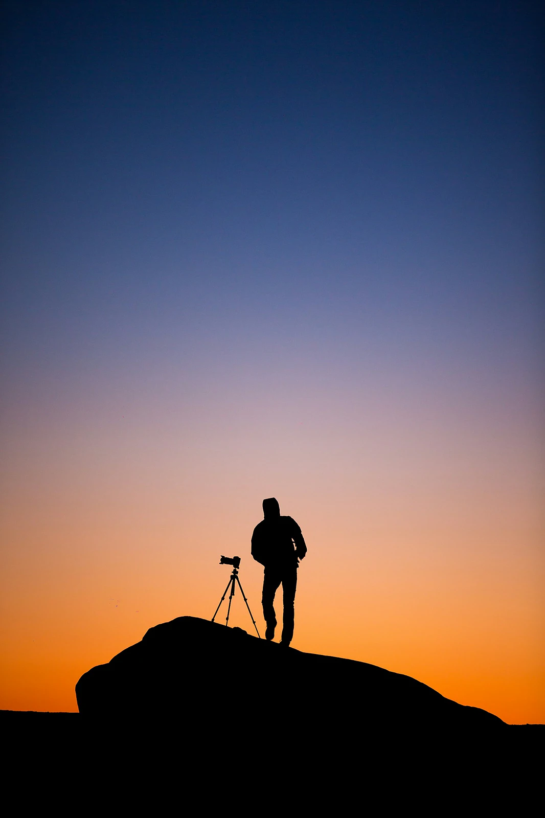 Photographer silhouetted beside a camera on a tripod at sunset