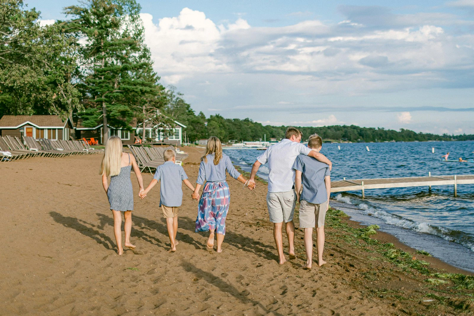 Family of five in soft blues and light neutrals holding hands while walking along a sandy beach